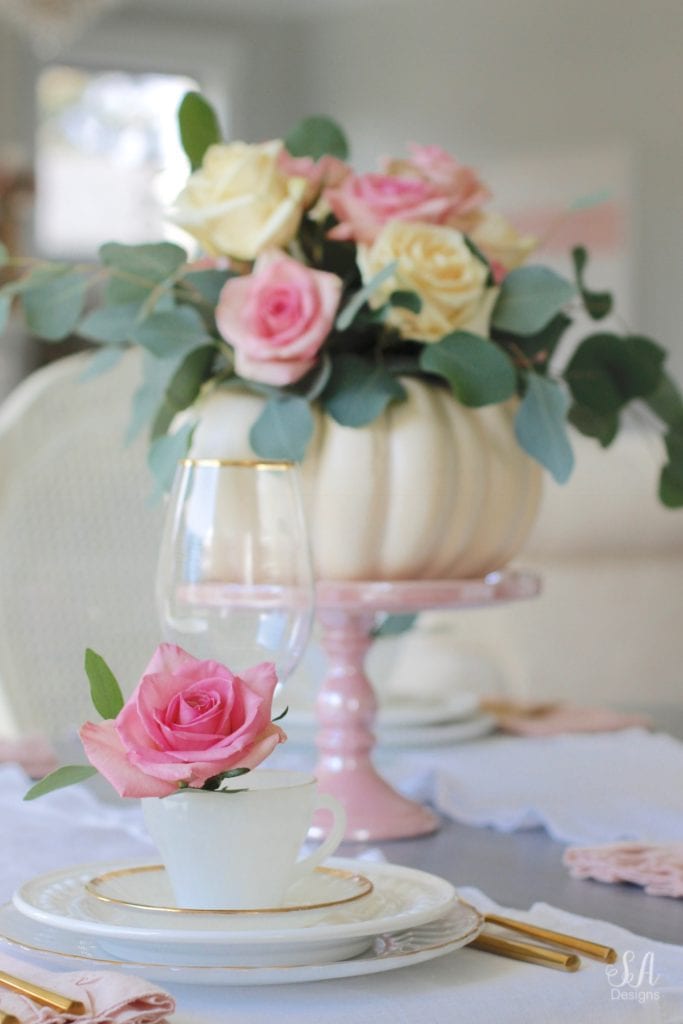 milk glass teacup, fresh pink roses, crystal chandelier, crystorama chandelier, white faux pumpkin floral arrangement, romantic floral brunch tablescape, girls table, brunch table, girlfriends party, fall party, fall tablescape, blush pink ruffle dinner linen napkins, white ruffle table runners, gold flatware, white beaded pottery barn dishes, white beaded world market dishes, gold rimmed goblets wine glasses, pink tablescape, pink table decor, place settings, vintage milk glass dinnerware