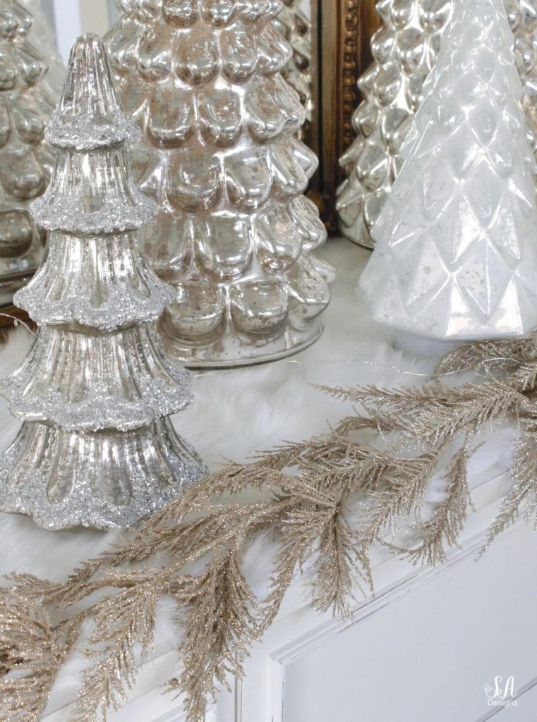 gold champagne glitter leaves garland Joanns fabrics, pottery barn mercury glass trees, anthropologie gleaming primrose glass mirror, elegant mixed metal decor, gold wreath, perigold dresser entry buffet table white transitional style buffet, michaels white faux fur christmas trees