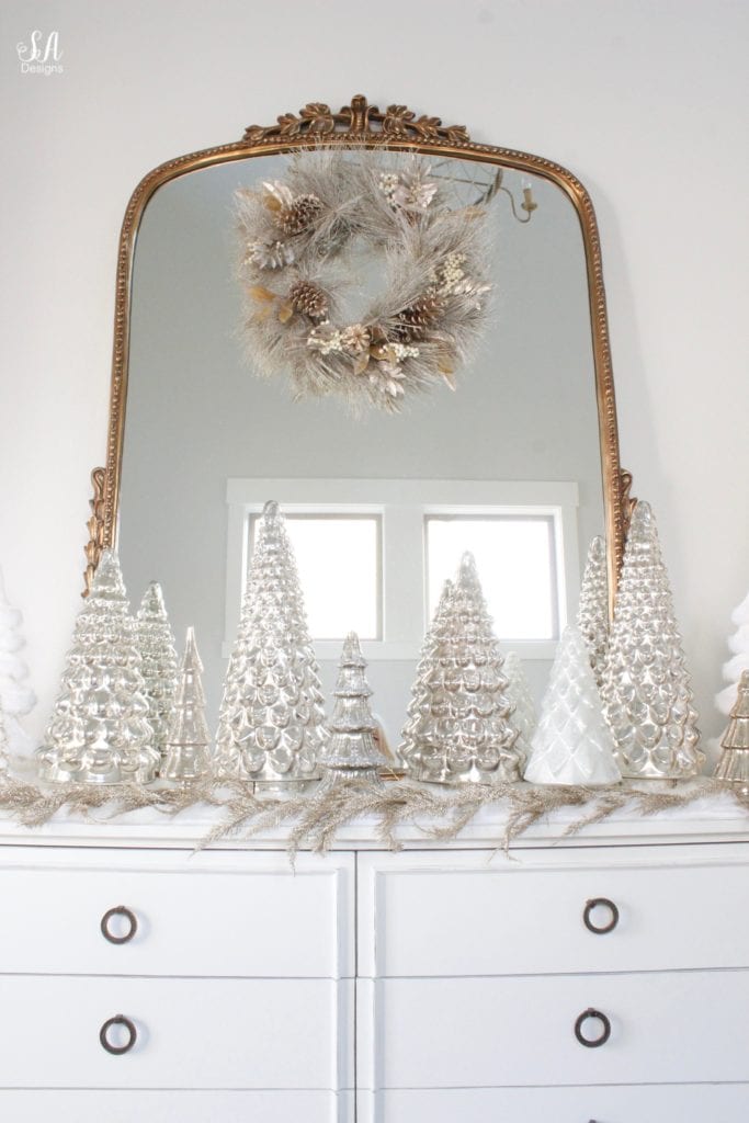 gold champagne christmas wreath gold leaves, pottery barn mercury glass trees, anthropologie gleaming primrose glass mirror, elegant mixed metal decor, gold wreath, perigold dresser entry buffet table white transitional style buffet, michaels white faux fur christmas trees