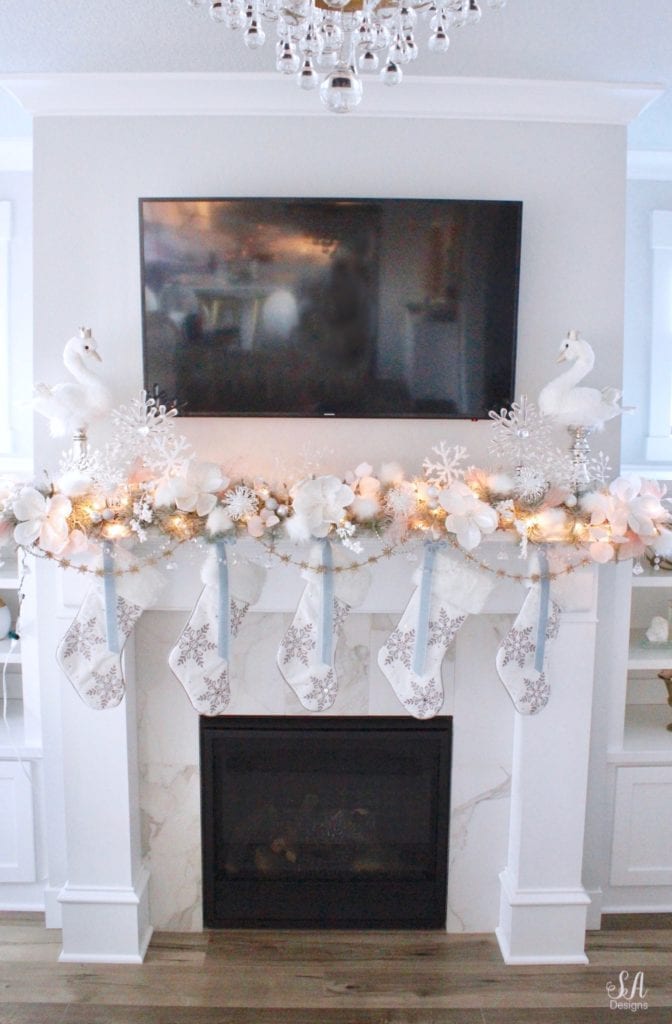 dreamy whimsical fantasy playful christmas mantel, faux fur stockings with snowflakes, christmas flocked garland with jewel rhinestone gold glitter pearl jewels garland, blush feather, faux fur pom poms, white glitter berry christmas stems, sparkly glitter christmas magnolia stems, dusty blue velvet ribbon, glitter snowflakes, joann fabric white swan figures, mercury glass candlesticks, cozy glam winter wonderland christmas, white fireplace marble tile