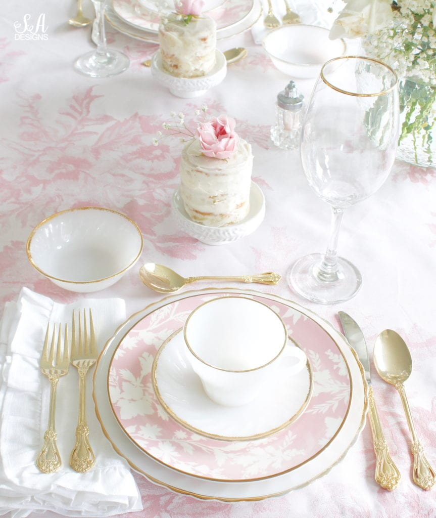 monique lhuillier pottery barn, pink floral tablecloth, pink floral plates, white kitchen design, vintage valentines day tablescape, valentines decor table, antique vintage milk glass plates teacups saucers gold rimmed, gold rimmed crystal goblets, vintage gold flatware, white ruffled napkins, individual mini naked cakes with fresh pink rose baby's breath