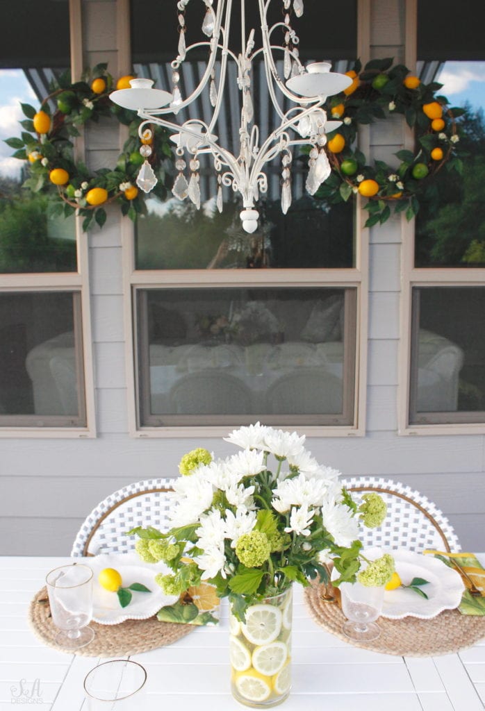 grey and white striped retractable awning, french outdoor patio, french style outdoor patio dining, french coastal backyard landscape dining outdoor design, english garden lemon tablescape, serena and lily outdoor umbrella, serena and lily grey white french bistro chairs, white oval outdoor dining patio table, outdoor patio table dining set, gold brass bar cart, lemon and fruit floral arrangement, outdoor patio chandelier, lemon tree