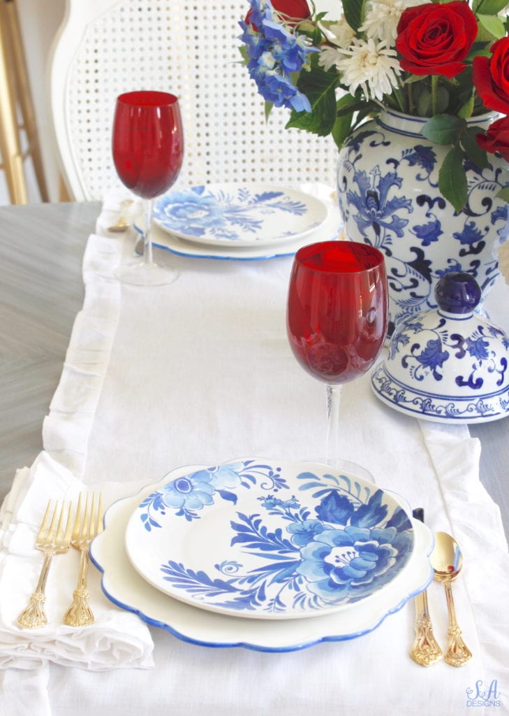 aerin plates williams-sonoma, scalloped blue rimmed plates, blue and white floral places,patriotic Tablescape, fourth of July table, red white and blue Tablescape table setting place setting, chinoiserie place setting, chinoiserie patriotic table, Aerin table place setting, Aerin plates Williams-Sonoma, scalloped plates, blue white plates, white ruffle dinner napkins, elegant gold flatware, red goblets, white ruffle table runners, white kitchen