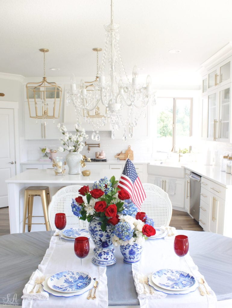 patriotic Tablescape, fourth of July table, red white and blue Tablescape table setting place setting, chinoiserie place setting, chinoiserie patriotic table, Aerin table place setting, Aerin plates Williams-Sonoma, scalloped plates, blue white plates, white ruffle dinner napkins, elegant gold flatware, red goblets, white ruffle table runners, white kitchen