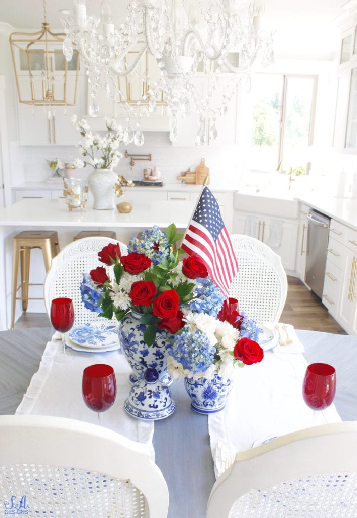 patriotic Tablescape, fourth of July table, red white and blue Tablescape table setting place setting, chinoiserie place setting, chinoiserie patriotic table, Aerin table place setting, Aerin plates Williams-Sonoma, scalloped plates, blue white plates, white ruffle dinner napkins, elegant gold flatware, red goblets, white ruffle table runners, white kitchen