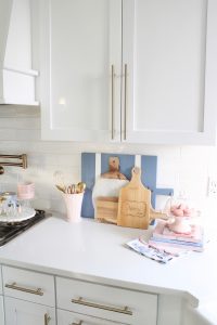 pink and blue spring kitchen decor, white kitchen design, white and gold kitchen, voluspa large 5 wick candle, voluspa macaron candles, white hood, white and gold kitchen, kitchen goals, Caitlin Wilson blue bread cutting board French blue, blogger kitchen inspiration, pink macarons on cake stand, pink and blue dessert books, recipe books to decorate with, dessert recipe books that are pink and blue to decorate your kitchen with