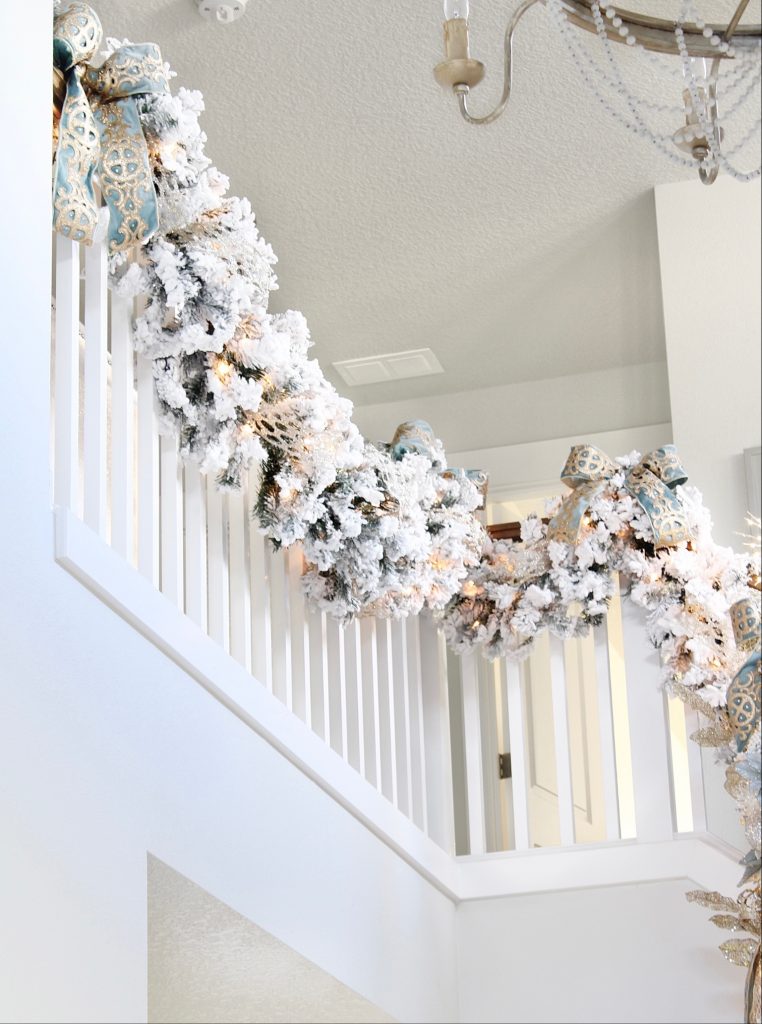 white flocked prelit christmas garland for banister staircase, trinity scroll velvet ribbon spa blue wired edge christmas ribbon, flocked christmas tree, glamorous christmas tree decorating tips, how to create a glam christmas tree, christmas decorating Tips, how to decorate a Christmas tree, elegant chic christmas tree entry, dramatic christmas entry, christmas tree stylist, blogger christmas tree, pottery barn mercury glass christmas trees