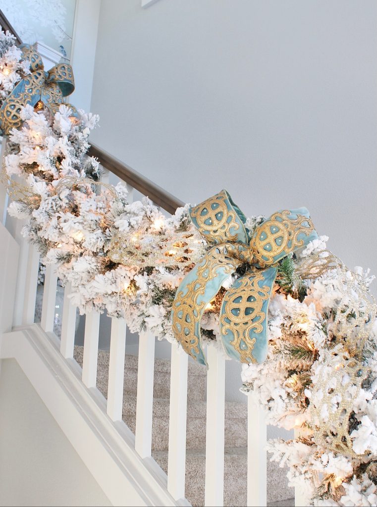 white flocked prelit christmas garland for banister staircase, trinity scroll velvet ribbon spa blue wired edge christmas ribbon, flocked christmas tree, glamorous christmas tree decorating tips, how to create a glam christmas tree, christmas decorating Tips, how to decorate a Christmas tree, elegant chic christmas tree entry, dramatic christmas entry, christmas tree stylist, blogger christmas tree, pottery barn mercury glass christmas trees