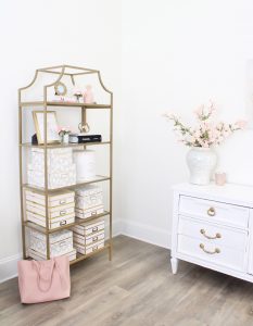 white and gold office, blush office, glam office, etagere gold shelves, Maltese dog, nesting boxes, home office, feminine office, diptyque candles used a flower vase, upcycled diptyque candle holder, white ginger jar pink cherry blossom stems, white matted gold frame set, office accessories, desk accessories, leopard slippers, white and gold leather office chair with wheels, pink pom pom throw blanket, blush tassel tote, gold office shelves, office shelving, how to decorate shelves, blogger office