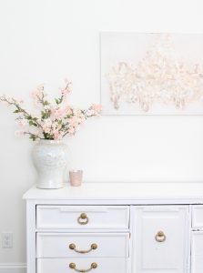 white and gold office, blush office, glam office, etagere gold shelves, Maltese dog, nesting boxes, home office, feminine office, diptyque candles used a flower vase, upcycled diptyque candle holder, white ginger jar pink cherry blossom stems, white matted gold frame set, office accessories, desk accessories, leopard slippers, white and gold leather office chair with wheels, pink pom pom throw blanket, blush tassel tote, gold office shelves, office shelving, how to decorate shelves, blogger office