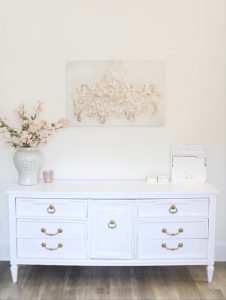 white and gold office, blush office, glam office, etagere gold shelves, Maltese dog, nesting boxes, home office, feminine office, diptyque candles used a flower vase, upcycled diptyque candle holder, white ginger jar pink cherry blossom stems, white matted gold frame set, office accessories, desk accessories, leopard slippers, white and gold leather office chair with wheels, pink pom pom throw blanket, blush tassel tote, gold office shelves, office shelving, how to decorate shelves, blogger office, Oliver gal candelabro canvas print