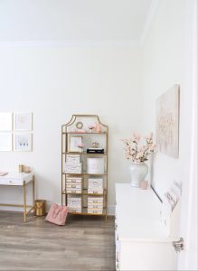 white and gold office, blush office, glam office, etagere gold shelves, Maltese dog, nesting boxes, home office, feminine office, diptyque candles used a flower vase, upcycled diptyque candle holder, white ginger jar pink cherry blossom stems, white matted gold frame set, office accessories, desk accessories, leopard slippers, white and gold leather office chair with wheels, pink pom pom throw blanket, blush tassel tote, gold office shelves, office shelving, how to decorate shelves, blogger office