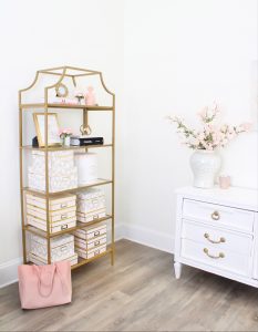 white and gold office, blush office, glam office, etagere gold shelves, Maltese dog, nesting boxes, home office, feminine office, diptyque candles used a flower vase, upcycled diptyque candle holder, white ginger jar pink cherry blossom stems, white matted gold frame set, office accessories, desk accessories, leopard slippers, white and gold leather office chair with wheels, pink pom pom throw blanket, blush tassel tote, gold office shelves, office shelving, how to decorate shelves, blogger office