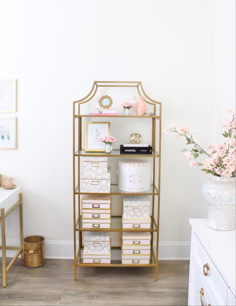 white and gold office, blush office, glam office, etagere gold shelves, Maltese dog, nesting boxes, home office, feminine office, diptyque candles used a flower vase, upcycled diptyque candle holder, white ginger jar pink cherry blossom stems, white matted gold frame set, office accessories, desk accessories, leopard slippers, white and gold leather office chair with wheels, pink pom pom throw blanket, blush tassel tote, gold office shelves, office shelving, how to decorate shelves, blogger office
