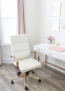white and gold office, blush office, glam office, etagere gold shelves, Maltese dog, nesting boxes, home office, feminine office, diptyque candles used a flower vase, upcycled diptyque candle holder, white ginger jar pink cherry blossom stems, white matted gold frame set, office accessories, desk accessories, leopard slippers, white and gold leather office chair with wheels, pink pom pom throw blanket, blush tassel tote, gold office shelves, office shelving, how to decorate shelves, blogger office